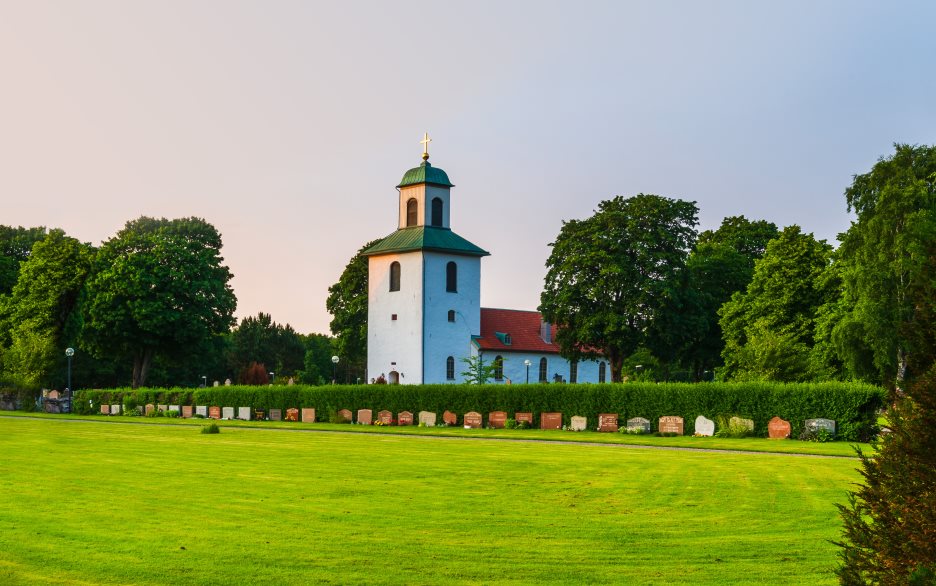 En vit landsbygdskyrka bland lummiga träd.