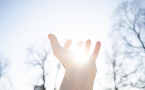 Någon håller upp en hand mot solen och det ser ut som att solen ligger i handflatan.