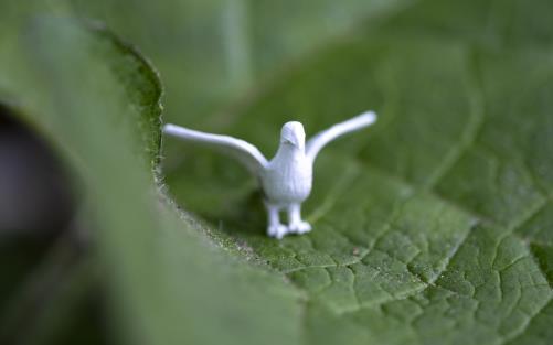 En liten vit plastduva med utsträckta vingar har placerats på ett grönt blad.