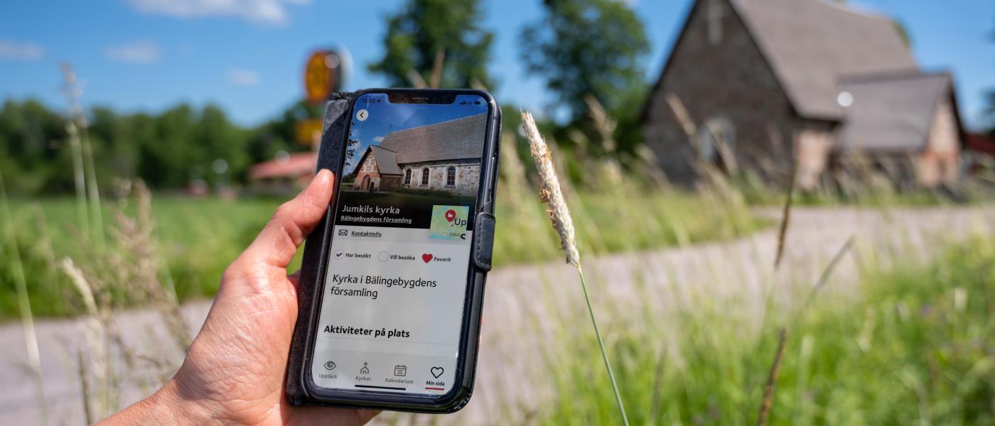 En hand håller i en mobil med skärmbild om kyrkguiden som visar adressen för kyrkan.