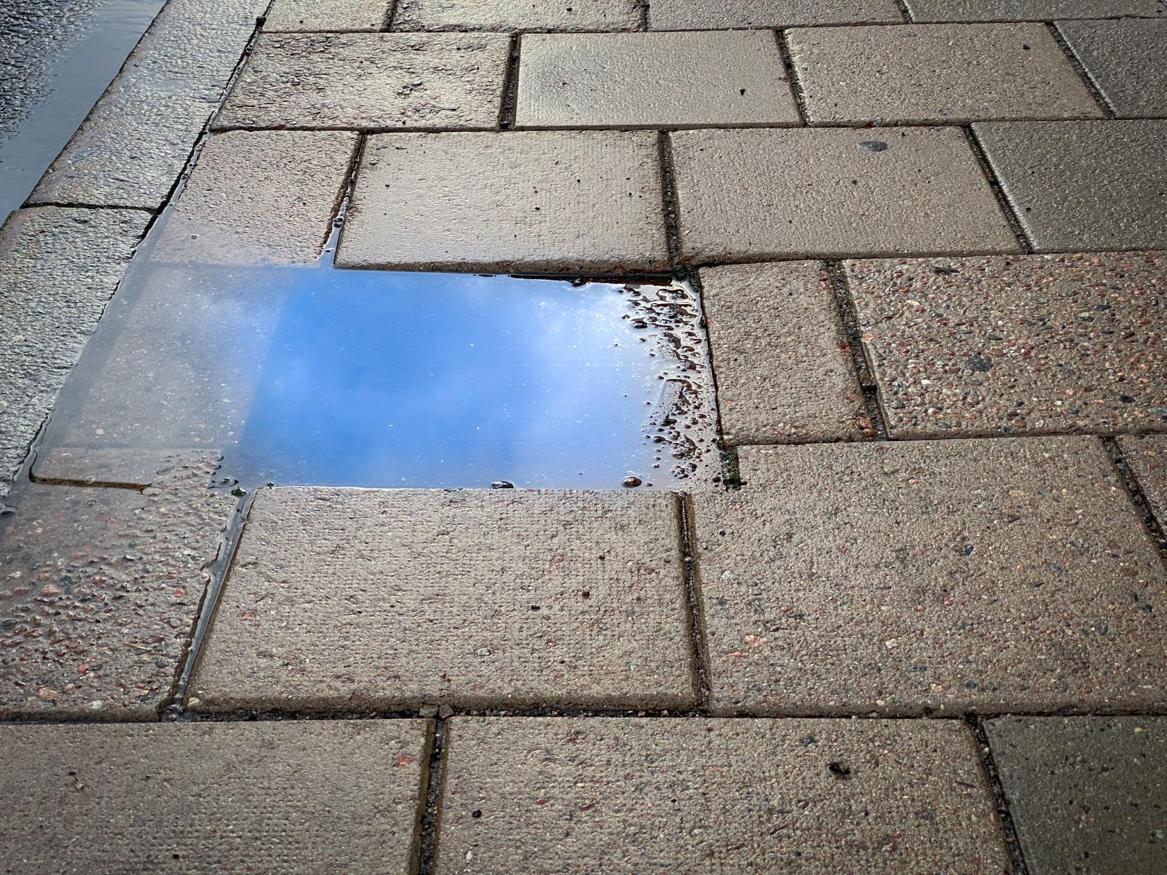 Himlen återspeglas i en vattenpöl på trottoaren.