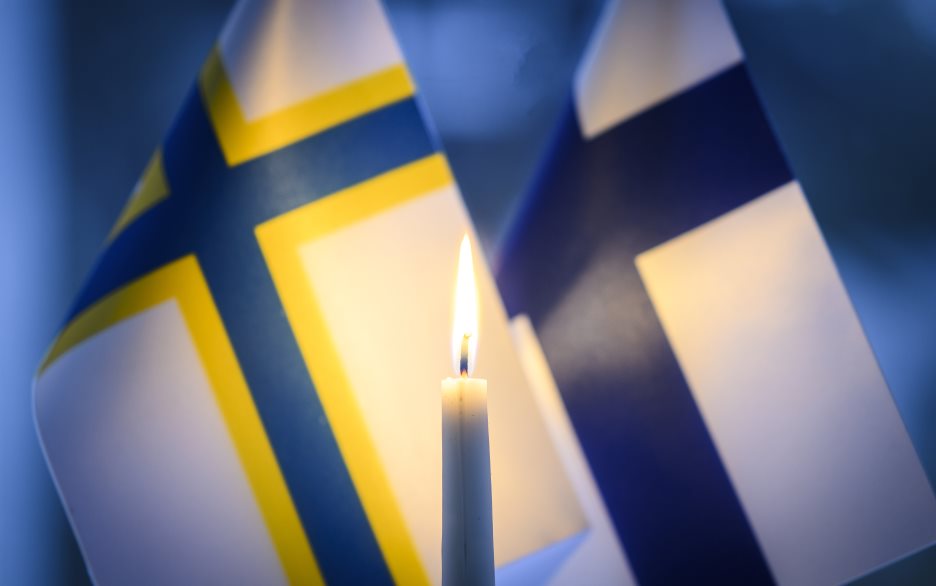 Ett stearinljus brinner framför en finsk och en sverigefinsk bordsflagga.