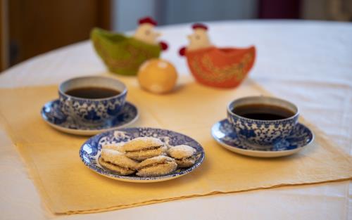 Ett kakfat, två kaffekoppar på fat och två påskhönor med ägg står uppdukade på en gul duk.