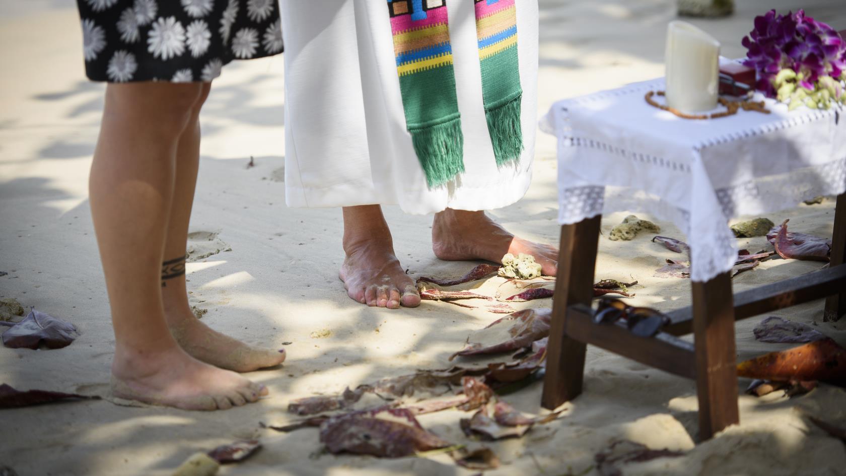 Präst och kvinna står barfota i sanden under en utomhusgudstjänst.