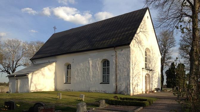 En vit stenkyrka med svart tak.