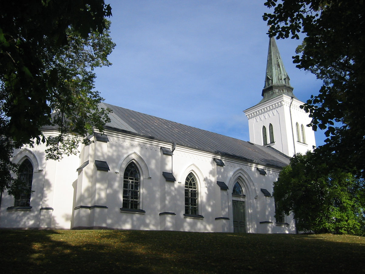 Östra Tollstads kyrka. En vit kyrka med långhus och torn. Blå himmel och gröna träd.