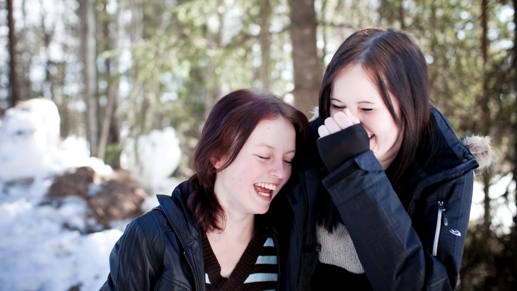 Två skrattande tonårstjejer i vårvinterskog