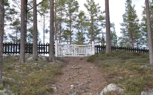 Ett spjälstaket med vit grind omger begravningsplatsen i Rullbo. 
