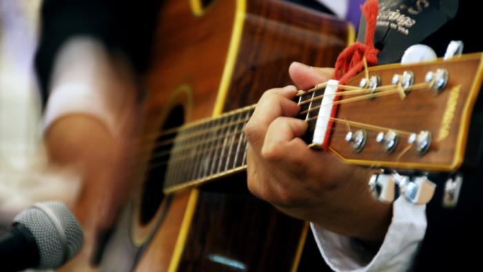 En person spelar på en akustisk gitarr. Bilden är beskuren så att bara gitarren och händerna syns.