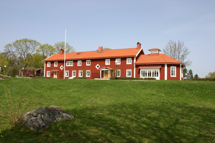 Röd trähuslänga mot blå himmel. Gräsmatta i förgrunden.