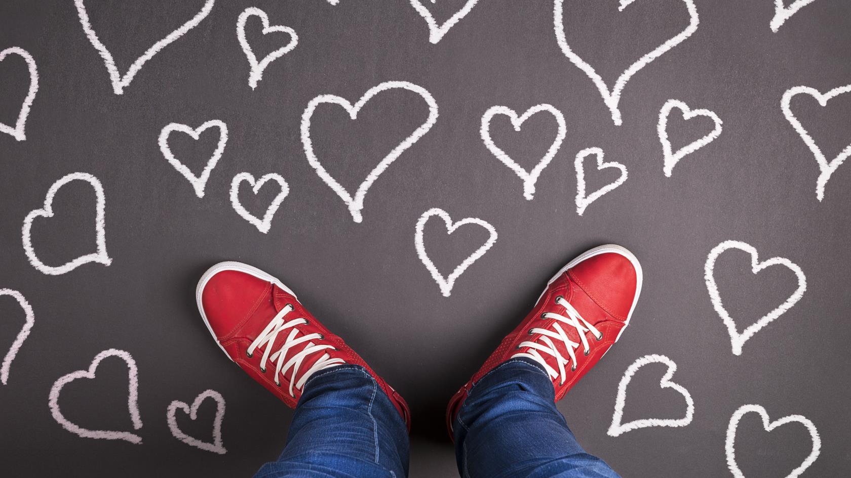 En person med röda skor och blå jeans står på en grå matta med vita hjärtan på. Bilden är tagen i fågelperspektiv så att bara ben och fötter syns.
