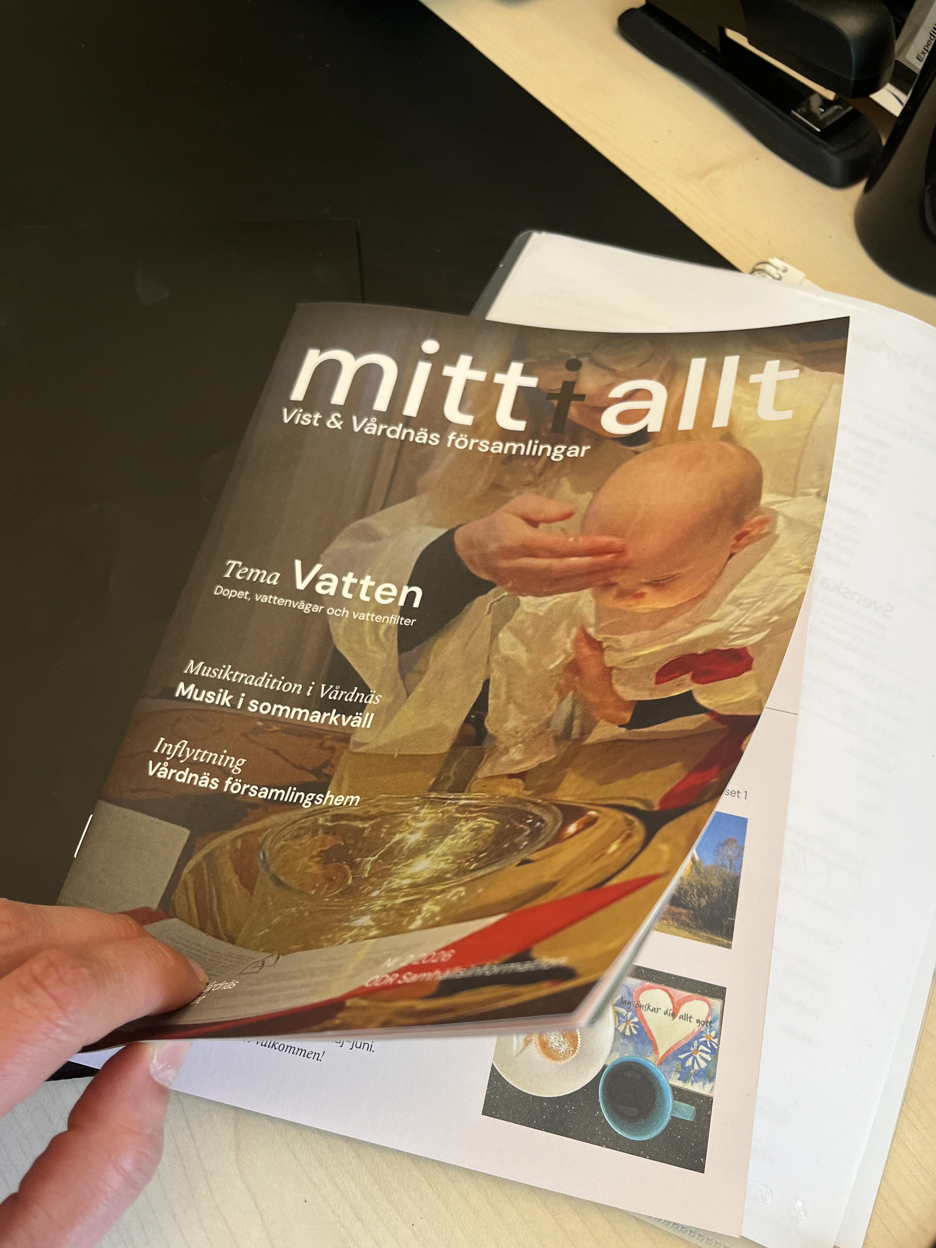 Bild på församlingsbladet "mitt i allt", någon bläddrar i den.