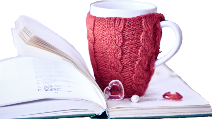 på en uppslagen bok står en kaffekopp med ett rosa stickat överdag