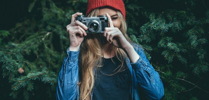 En fotograf i röd mössa riktar kameran mot dig