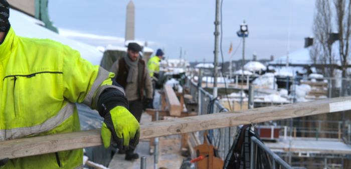 Det är 11 grader minus och det har precis slutat snöa. Raskt är alla på Storkyrkans tak ca 40 meter över mark. Det är takläggning av plåt, byte av högbenet i en takstol och förberedelser för resning av byggnadsställningar runt tornet. Under den inplastade delen har putsningen framskridit. Vi kikar in på bygget under två dagar i början på februari och får träffa timmermännen som ska byta ut ett högben i en 1700-tals takstol.