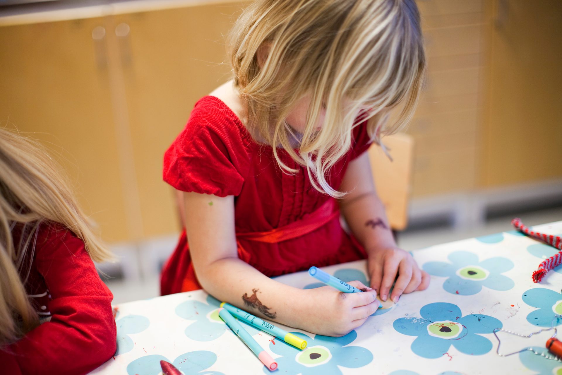 En flicka i röd klänning sitter och ritar.