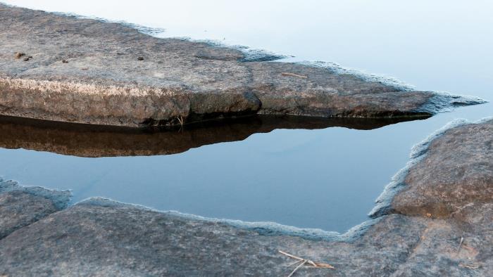 En klippskreva med vatten. Utanför syns havet.