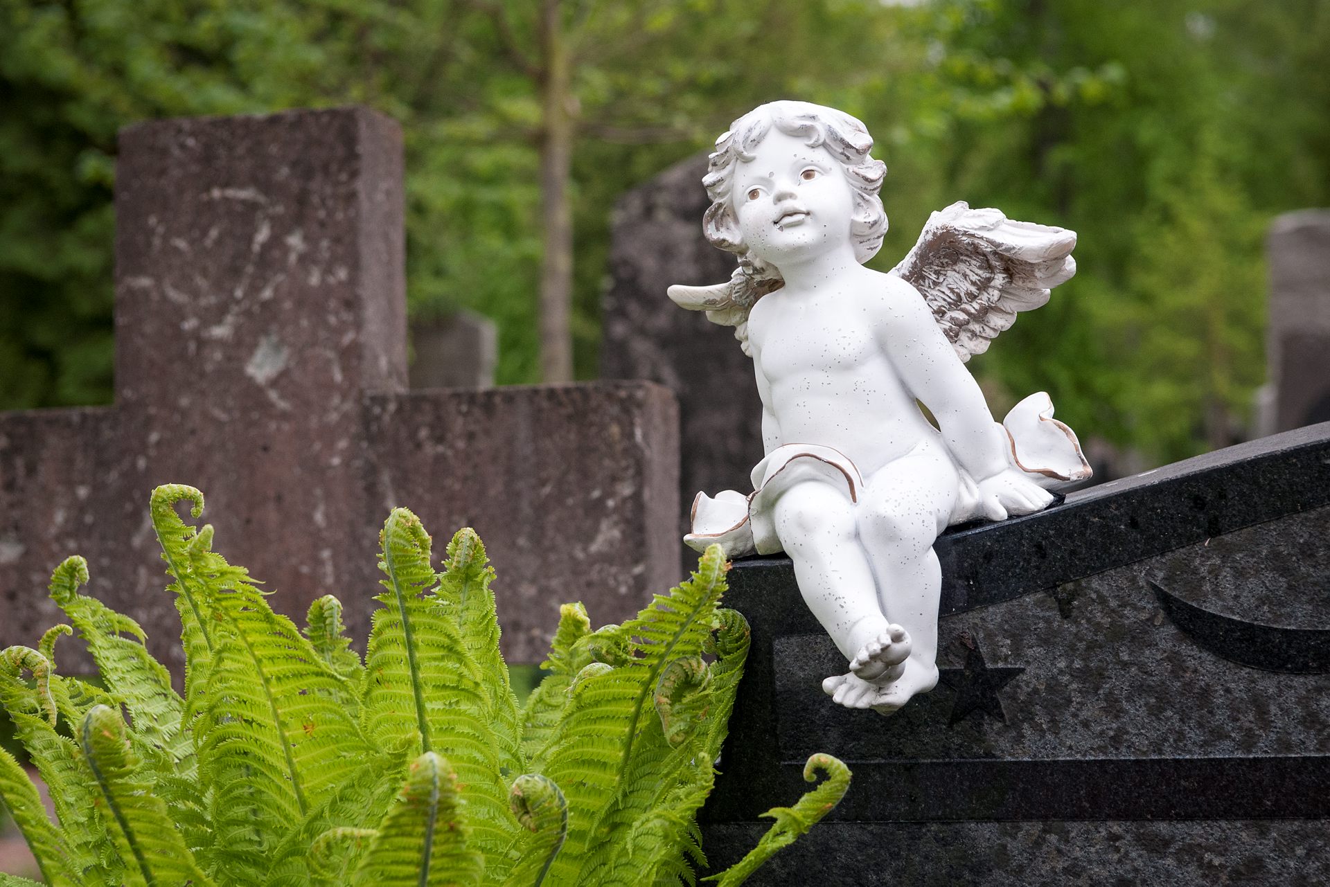 Ängel i sten som sitter på en gravsten.
