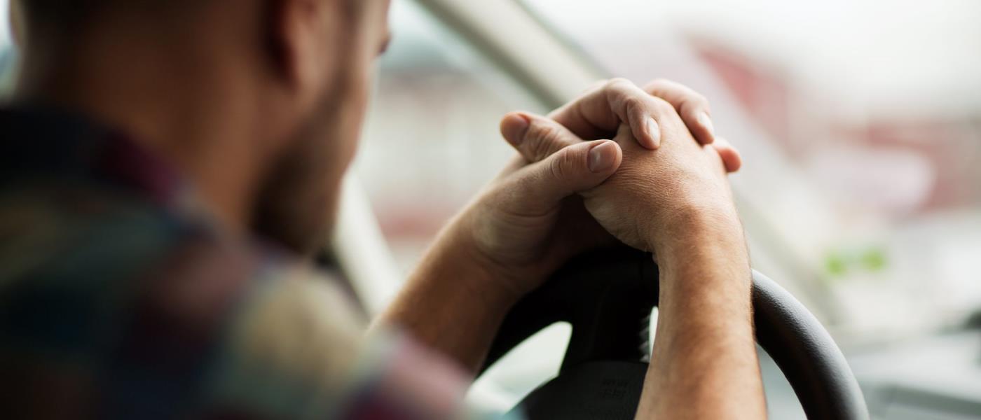 En man håller händerna knäppta i bön över ratten i sin bil