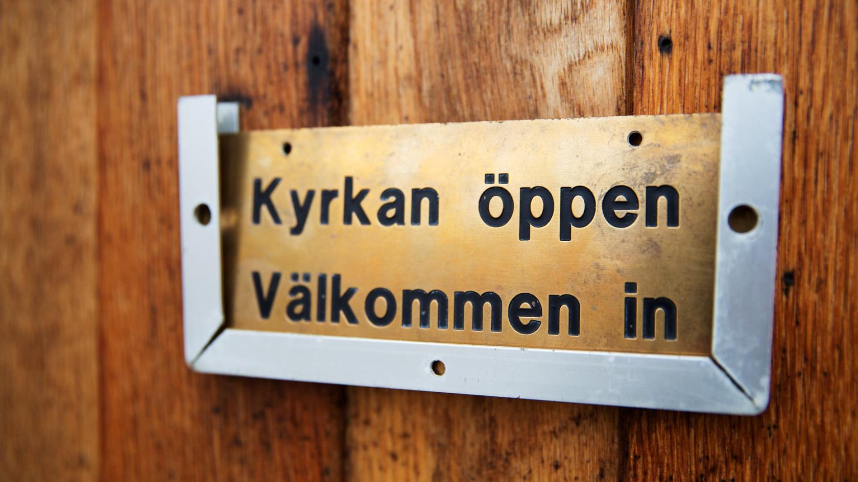 Dörrskylt med texten "Kyrkan öppen, välkommen in".