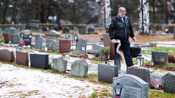 Kyrkogårdsvaktmästare sandar gångarna på kyrkogård.