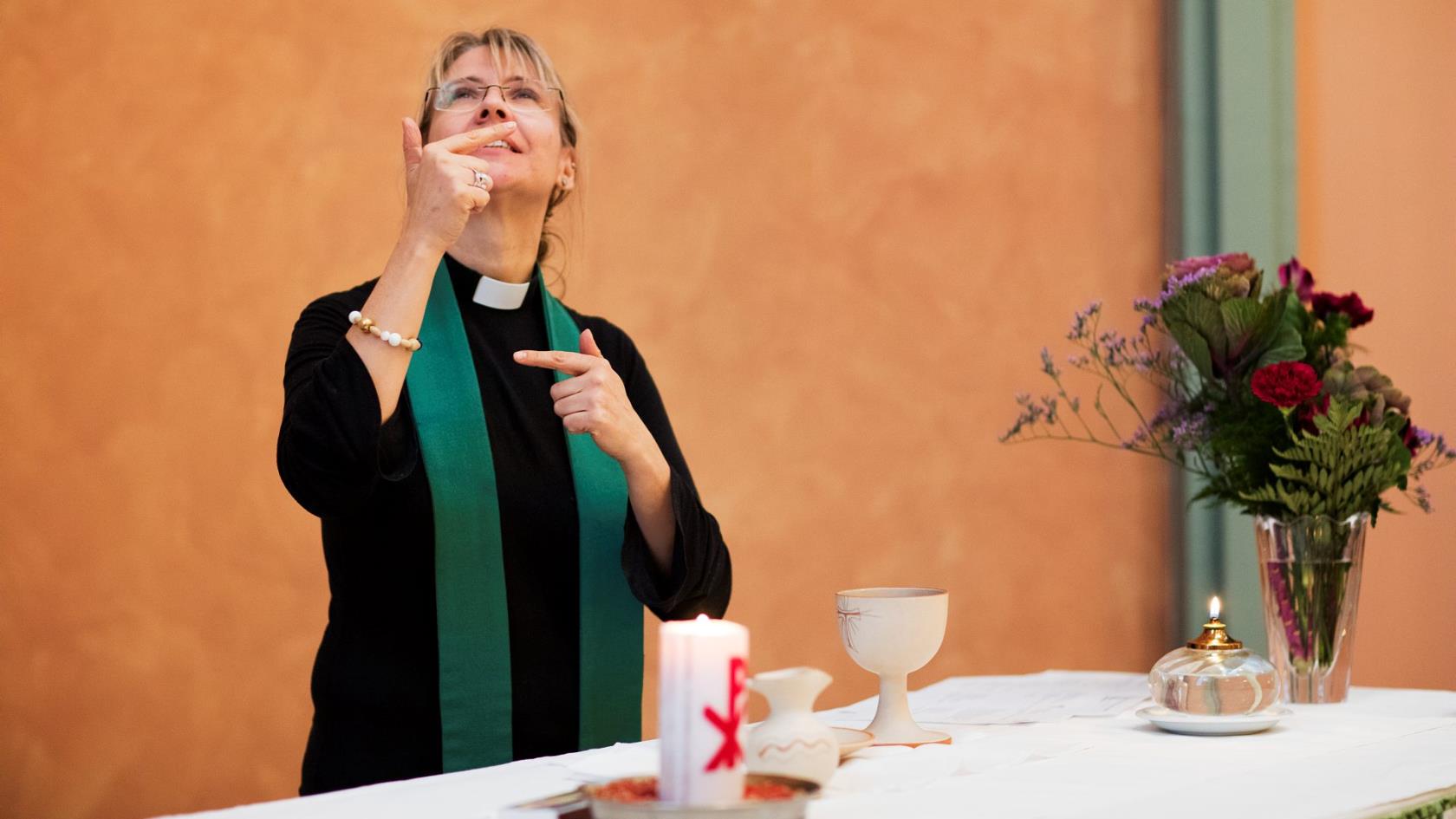 Präst vid altarbord som tecknar på teckenspråk.
