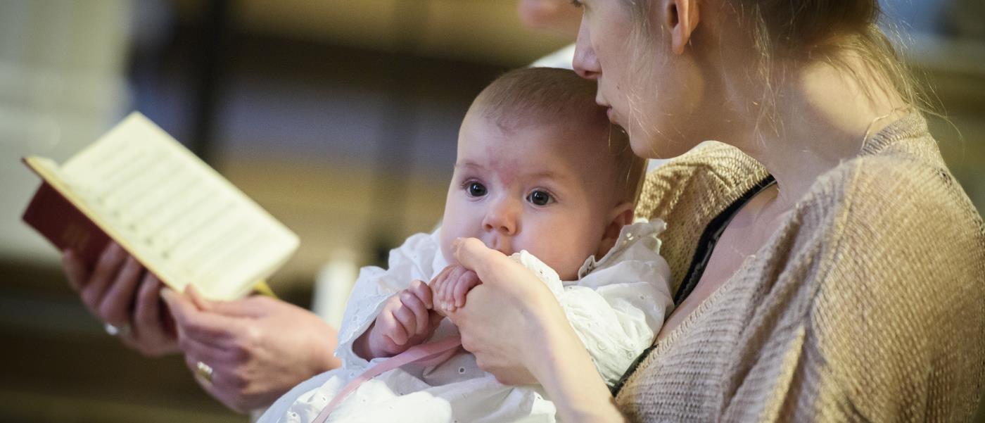 Mamma håller bebis under ett dop.