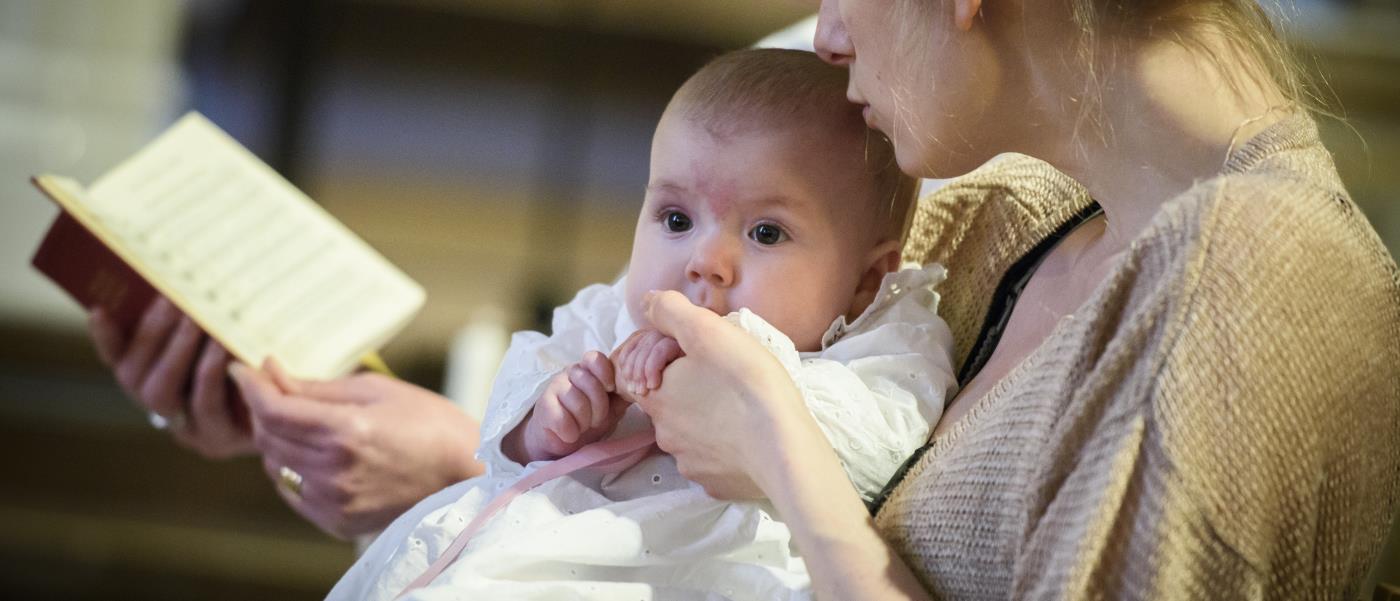 Mamma håller bebis under ett dop.