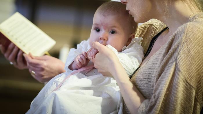 Mamma håller bebis under ett dop.