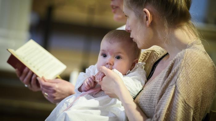 Mamma håller bebis under ett dop.