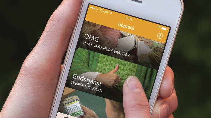 Ett par händer som håller i en mobiltelefon som visar Kyrkguiden. 