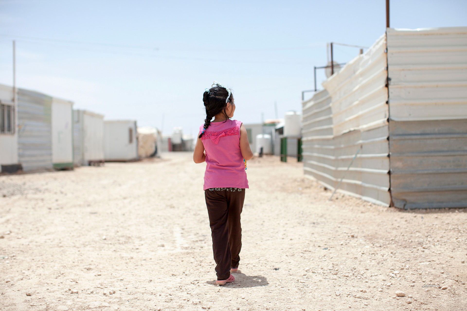 Flicka i rosa tröja går längs en gata i flyktinglägret. 