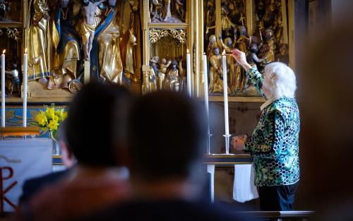 Äldre kvinna tänder höga ljus längst fram i kyrkan.