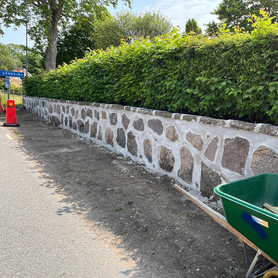 En nymurad vit mur runt en kyrkogård. I muren är det insprängt stora stenar.