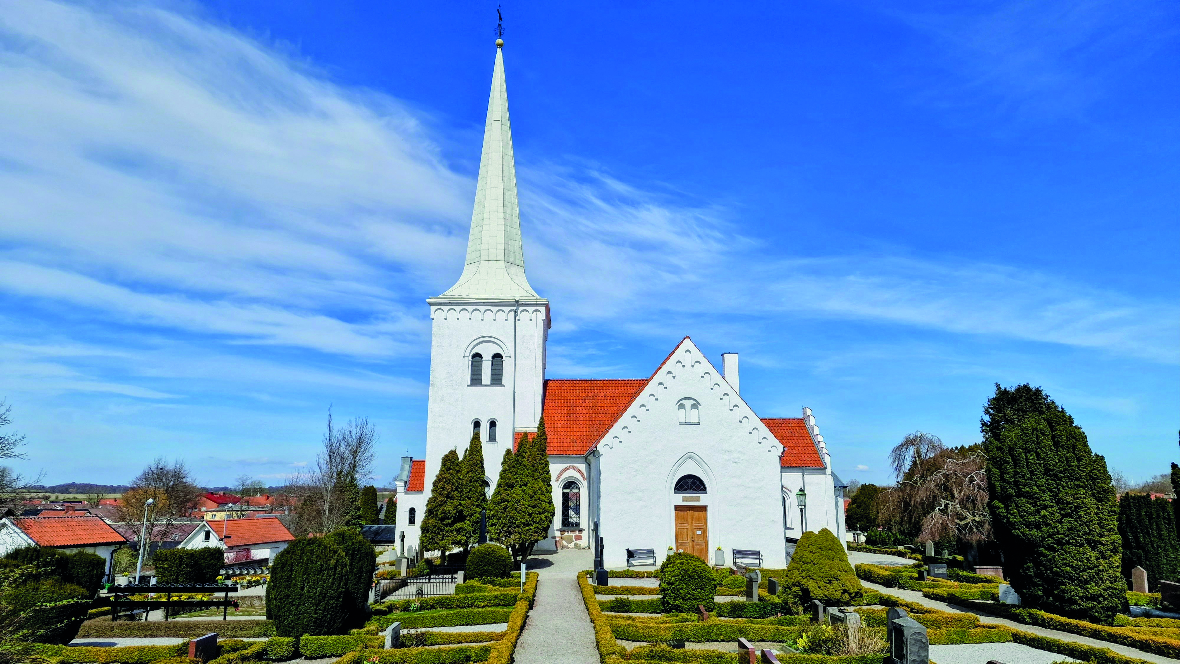 Anderslöv vita stenkyrka i en somrig kyrkmiljö.