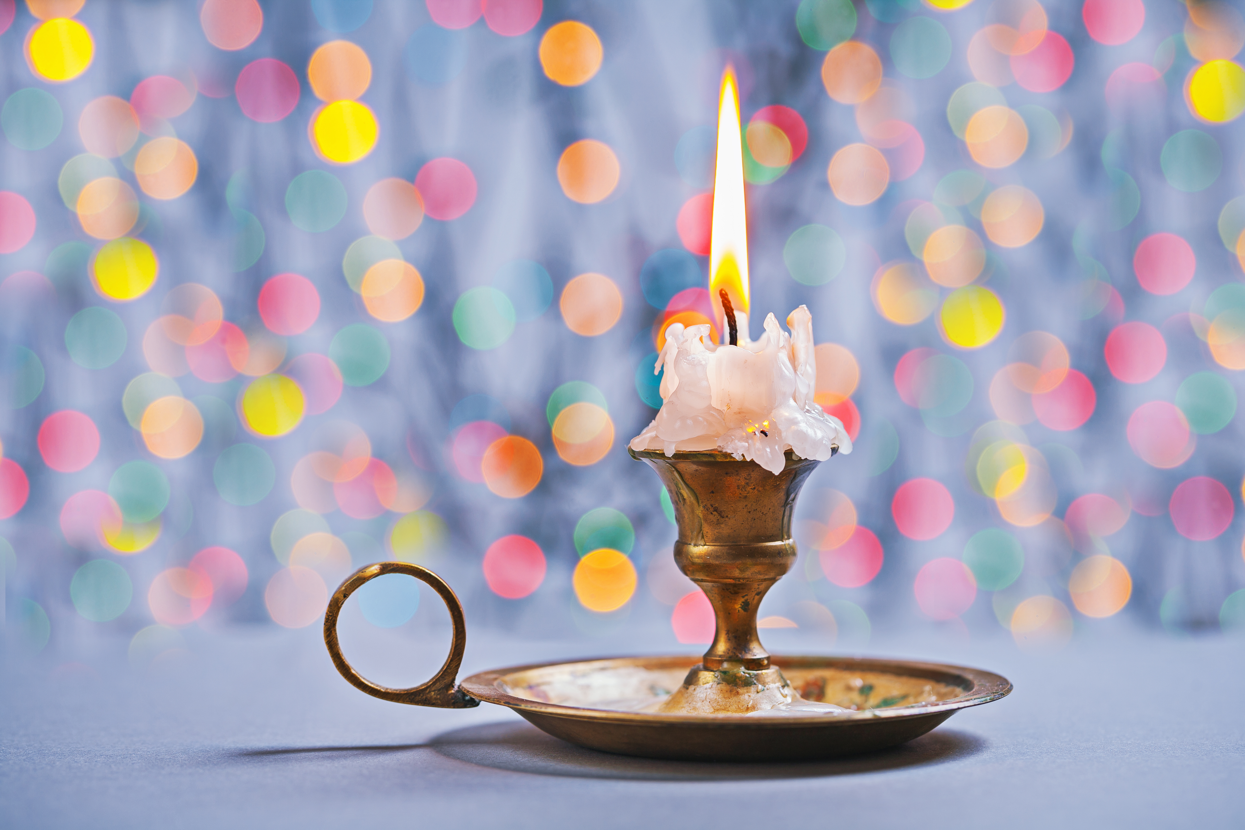 En brinnande ljus i en mässingsljusstake. Färgglada prickar i bakgrunden. 