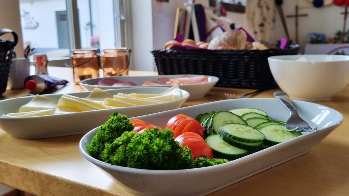 En uppdukad frukostbuffé med grönsaker, ost & skinka på olika fat.