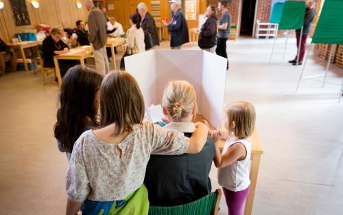 Röstande i en vallokal 2017. En mamma röstar i valbåset omgiven av tre barn.