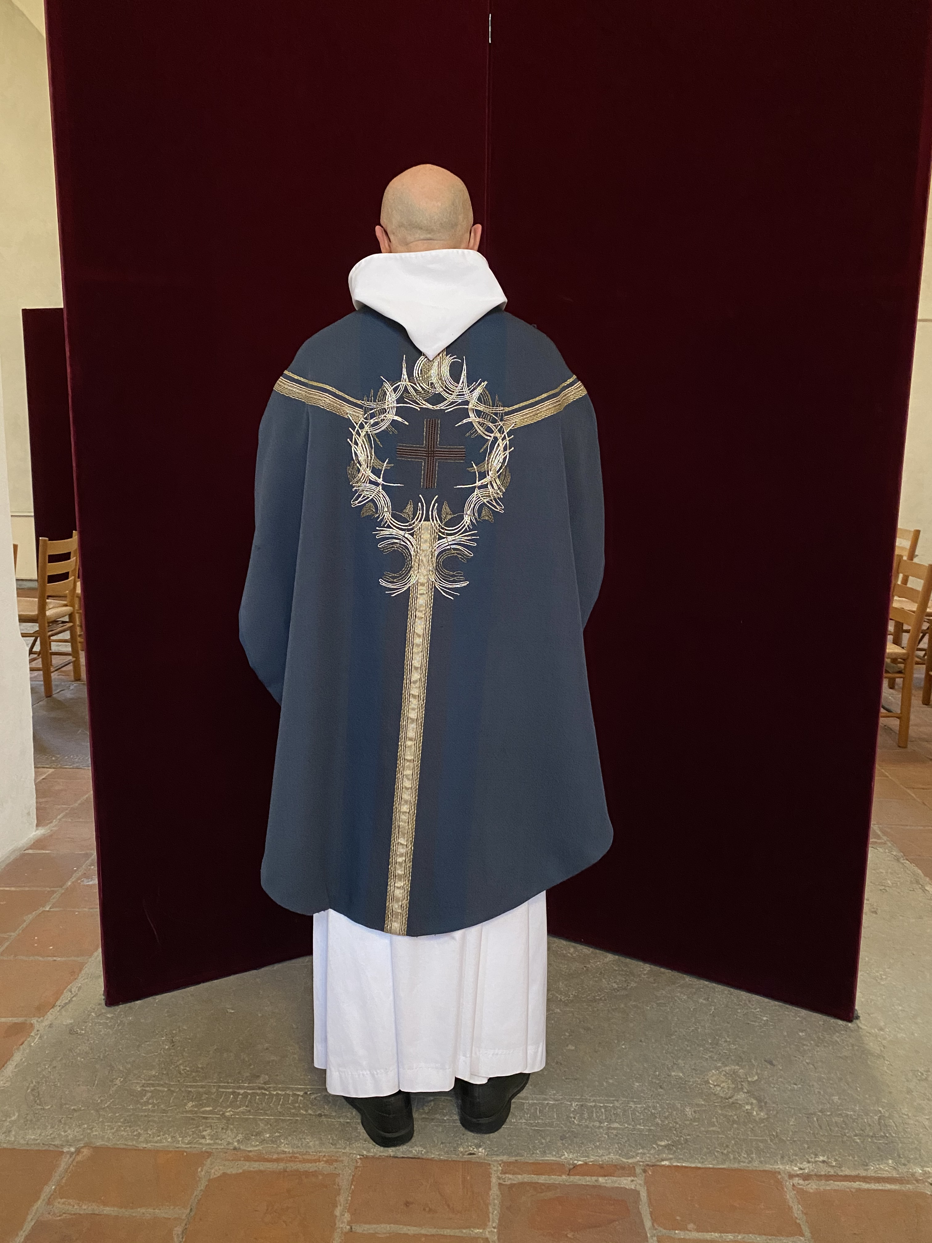 Präst klädd i alba och blå mässhake, dekorerad på ryggsidan.