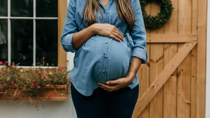 Gravid kvinna i blå skjorta håller händerna runt den runda magen