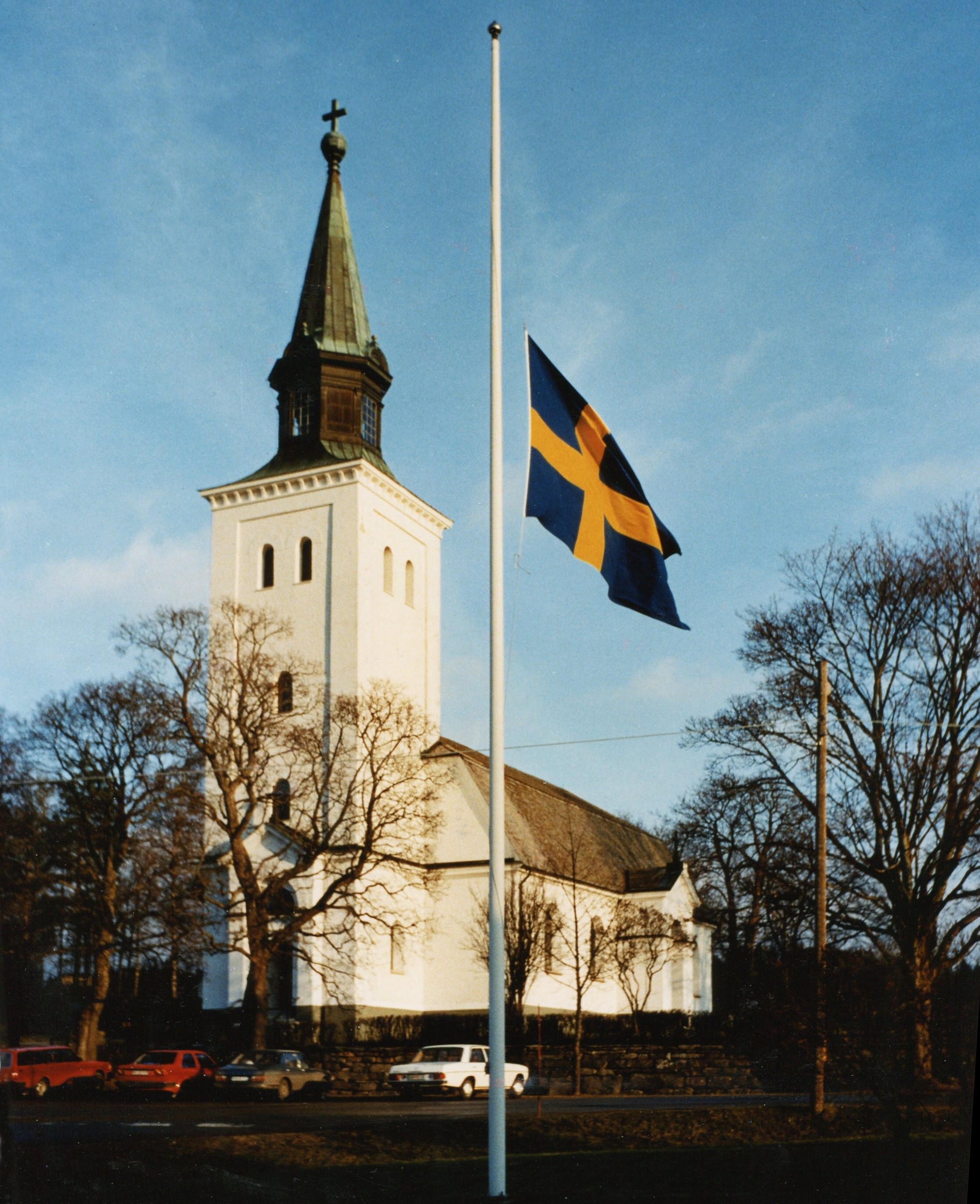 Flagga på halv stång vid ett vitt kyrktorn