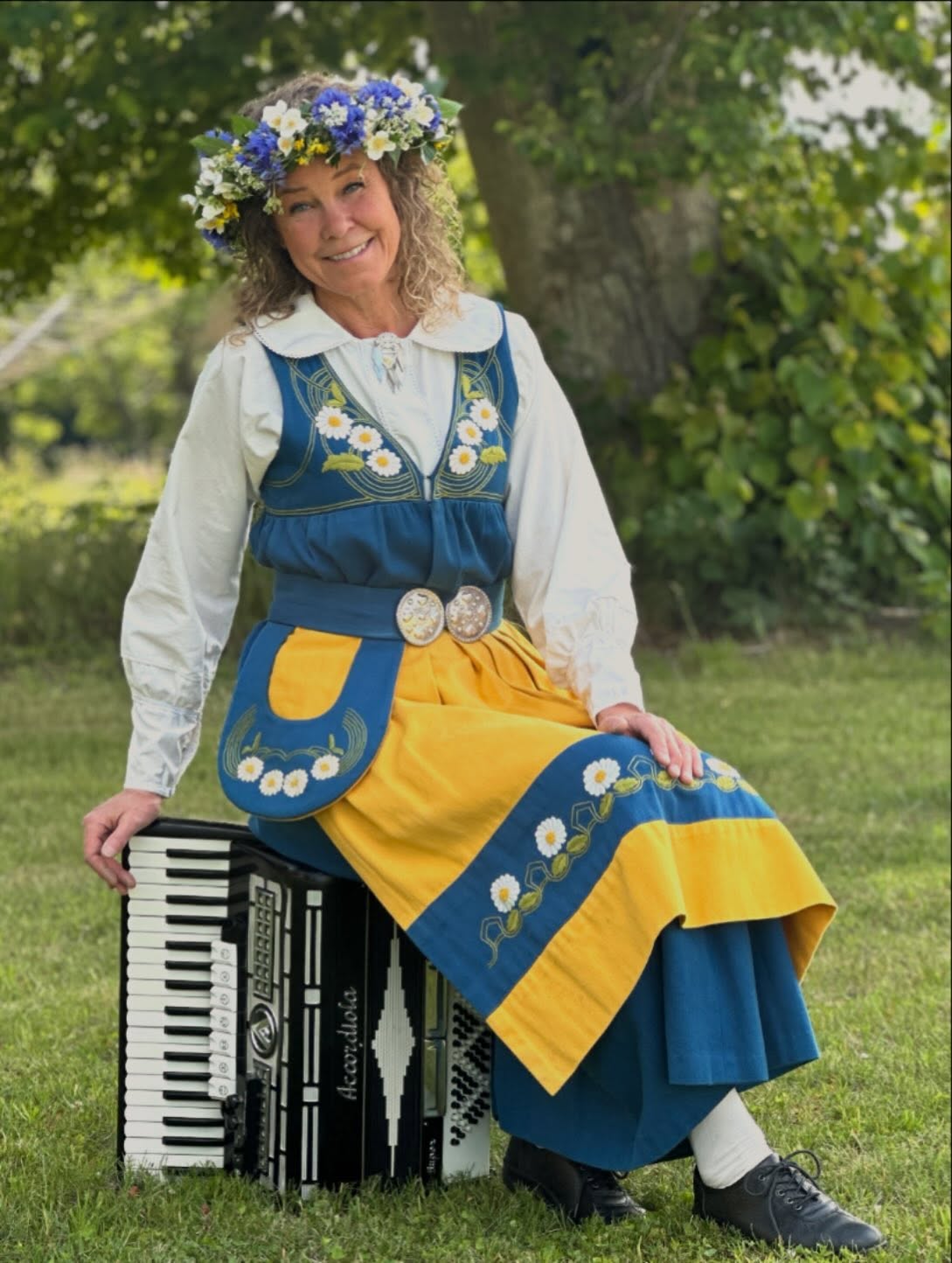 En kvinna i Sverigedräkt och blomsterkrans sitter på ett dragspel