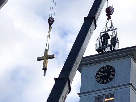 Ett guldkors hänger i en lyftkran på väg ner från ett kyrktorn