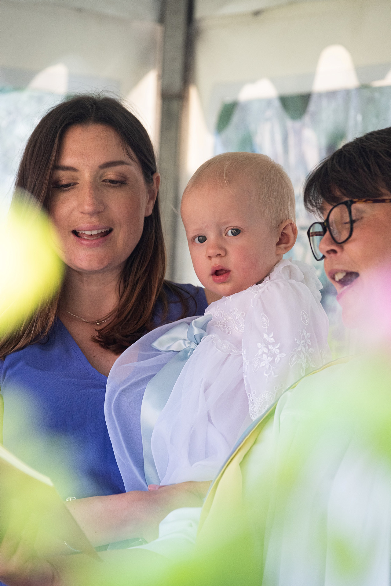 Två kvinnor och ett barn i dopdräkt med sommarfärger.