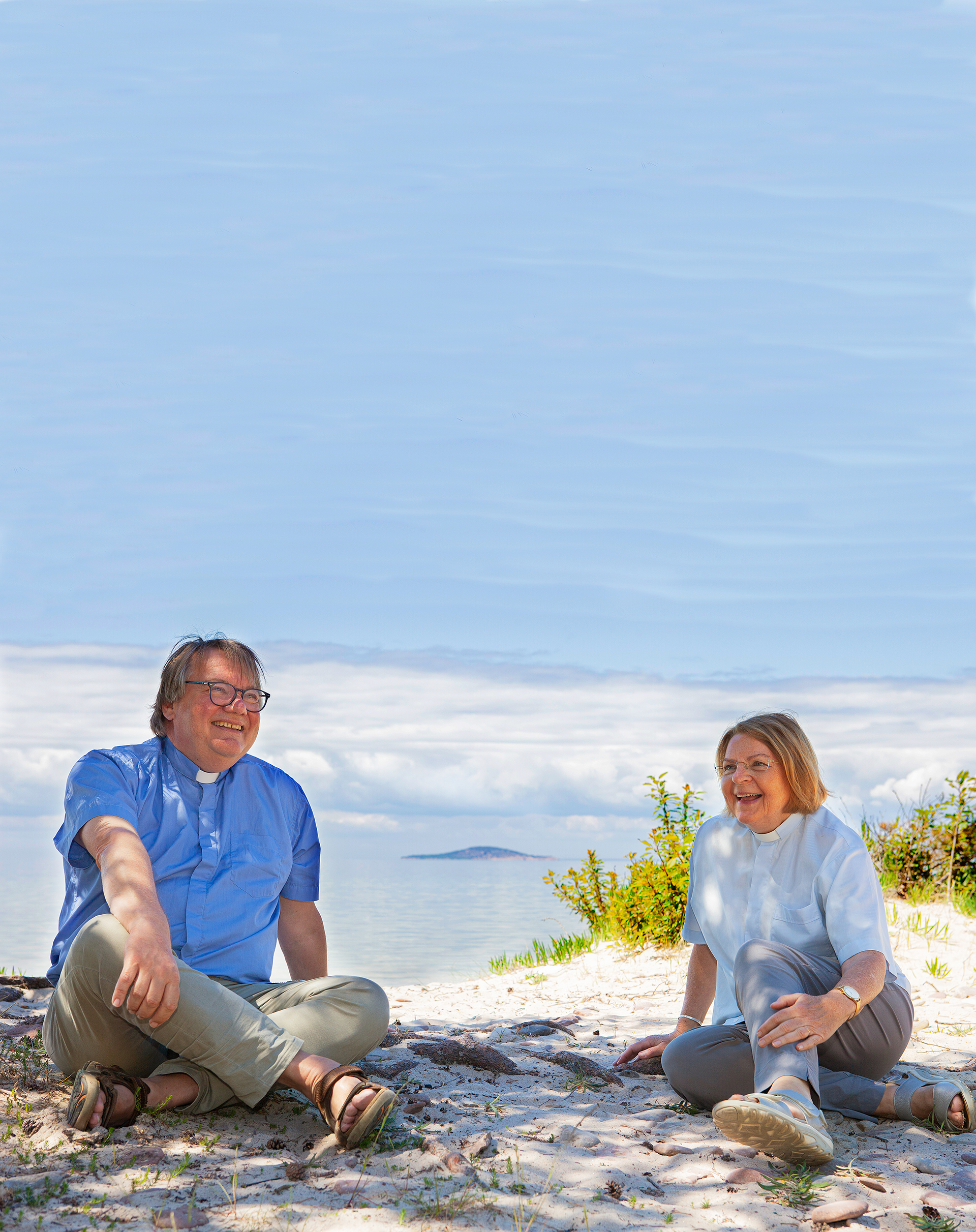 Två präster sitter på en strand med havet i bakgrunden