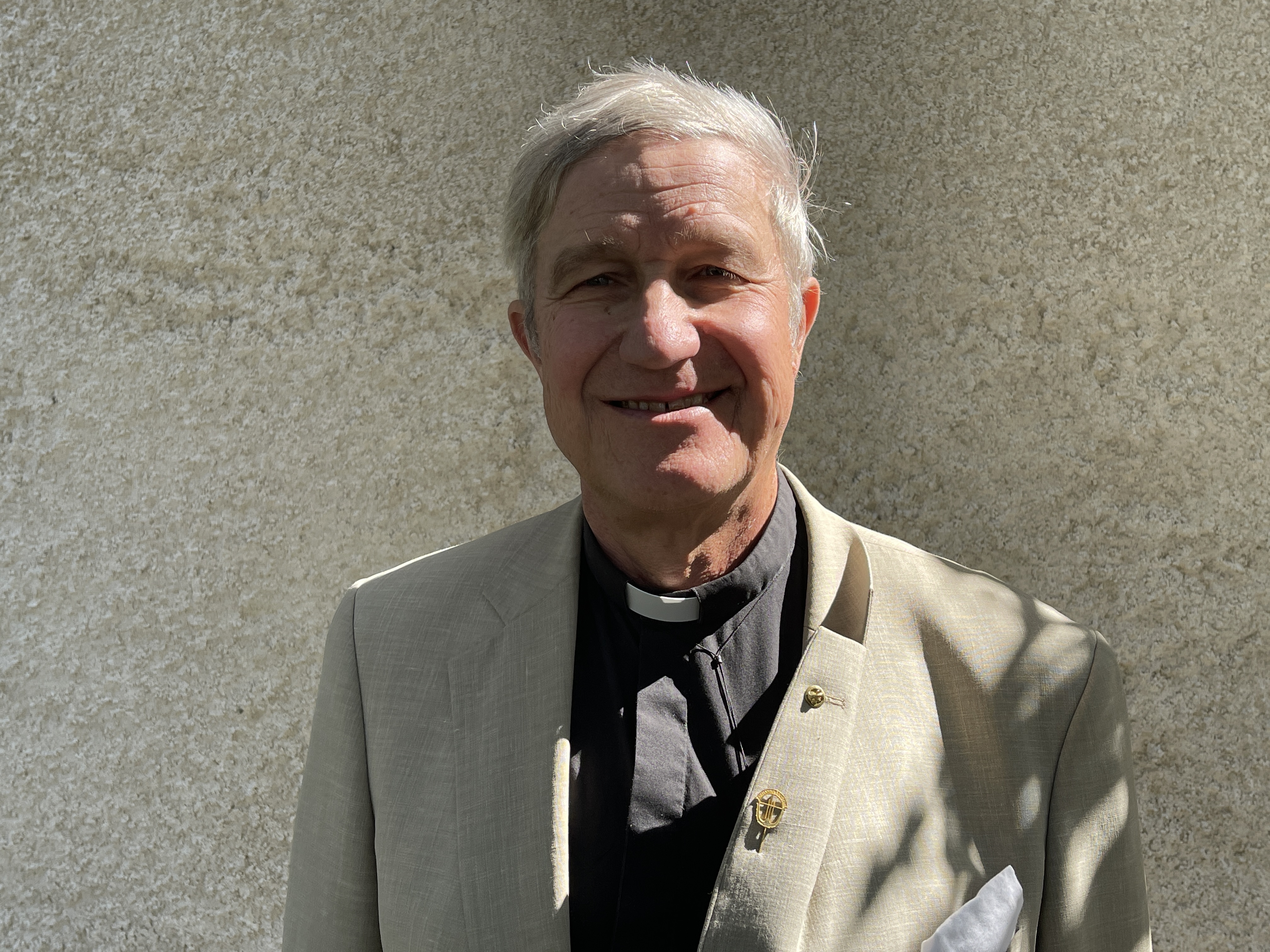 Foto av prästen Henrik Hammar i ljus kostym