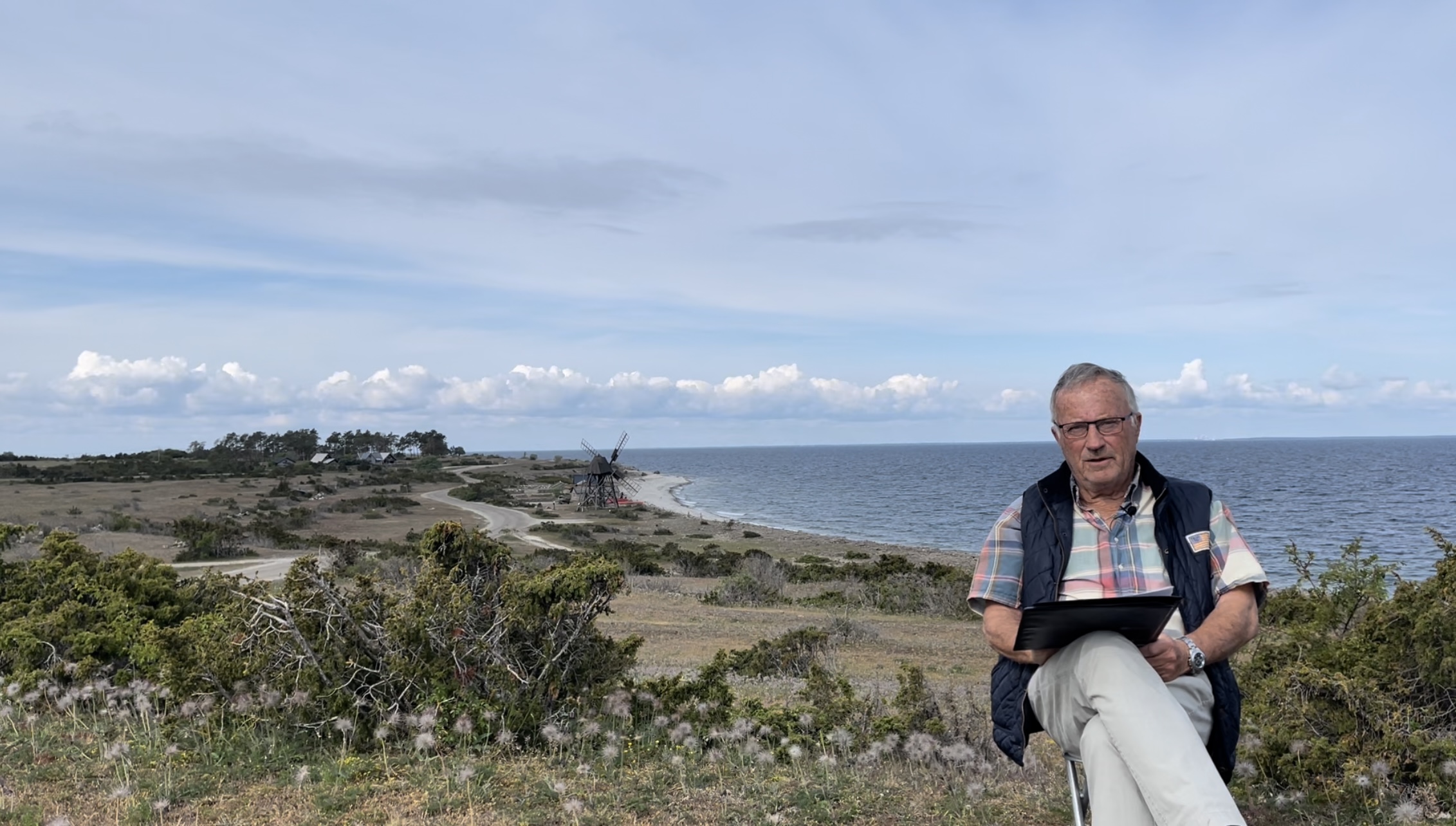 Man sitter på en höjd med havet och en skurkvarn bakom sig.