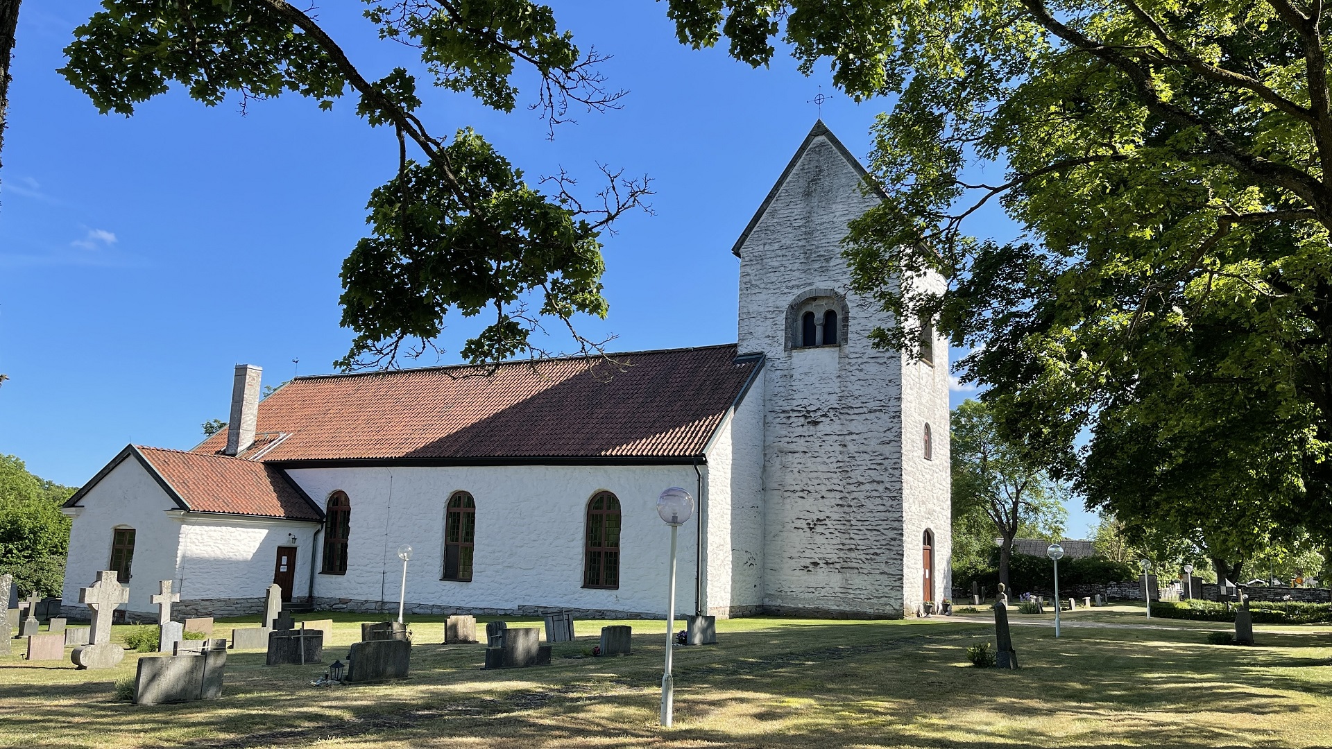 Vit kyrka med rött tak. Träd i förgrunden.
