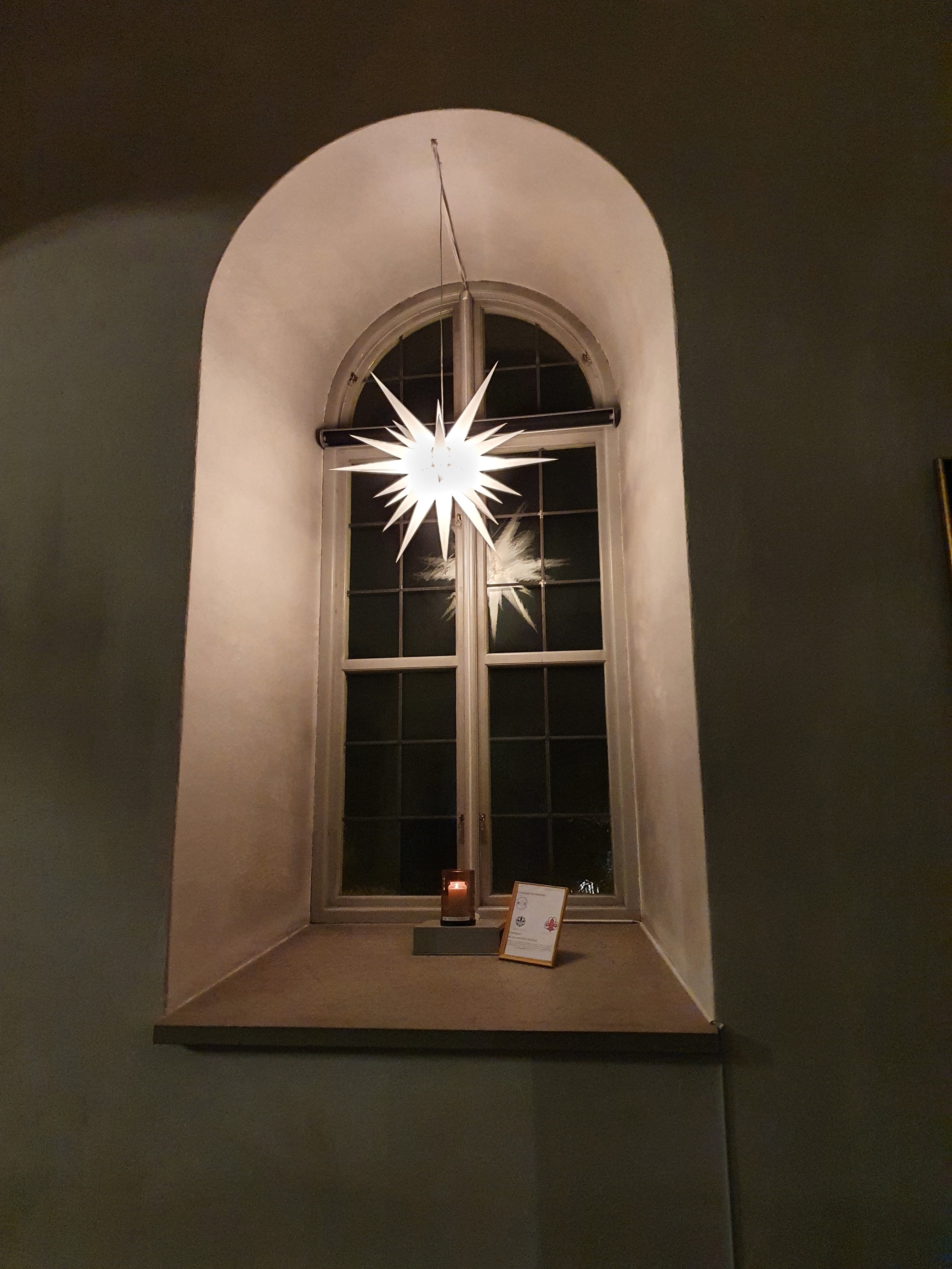 Ljus brinner i ett kyrkfönster under en stjärna