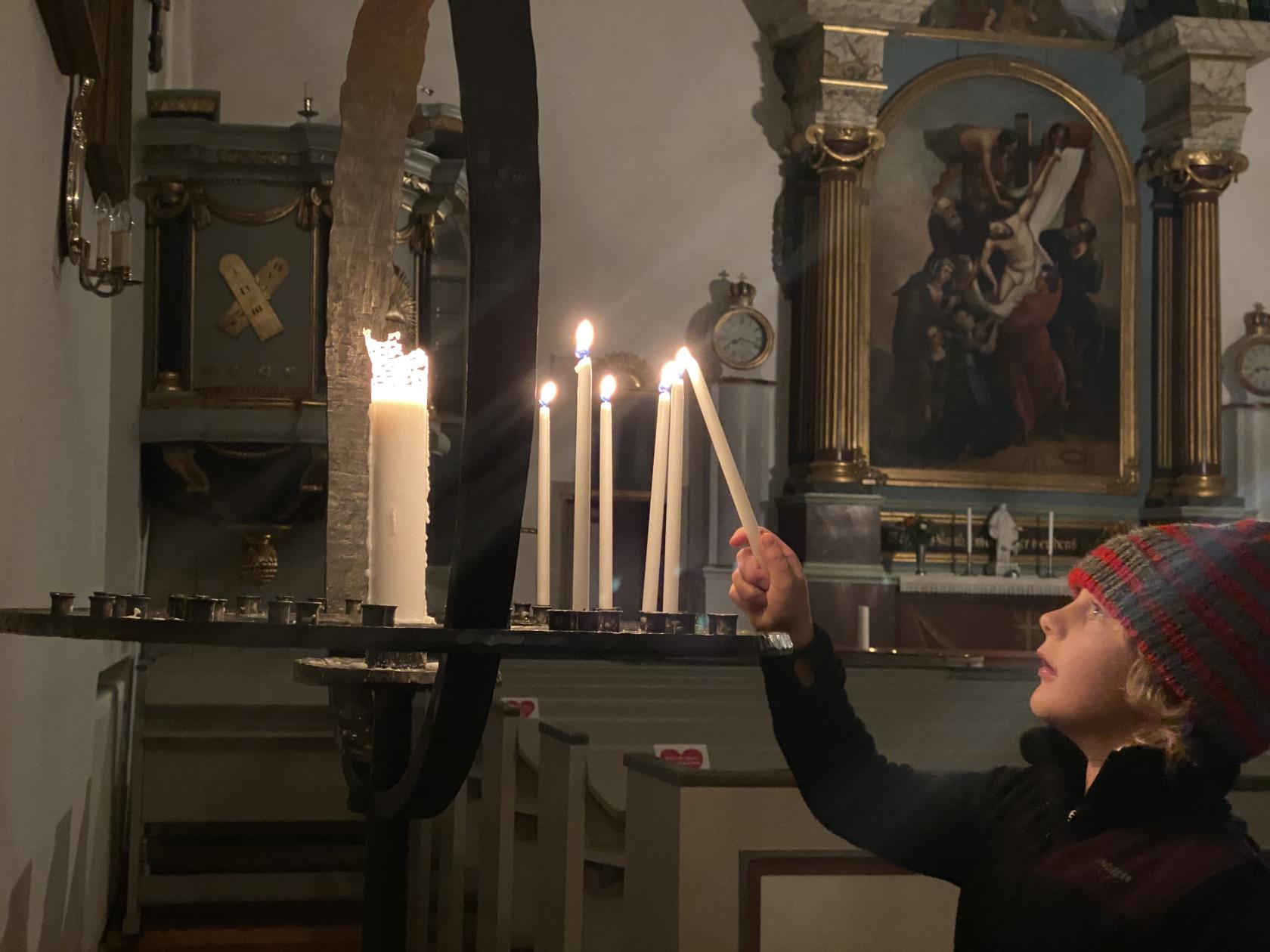 En pojke tänder ett ljus i en ljusbärare i en kyrka